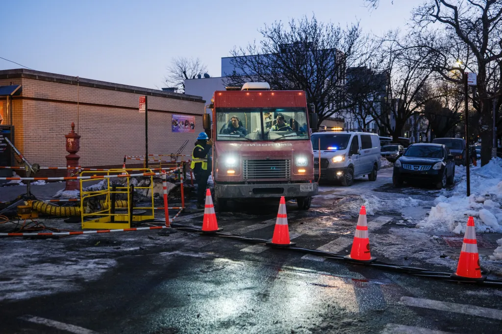 Con-Ed workers restoring power on a snowy street in Bushwick after a fire, with work vehicles and orange cones present.