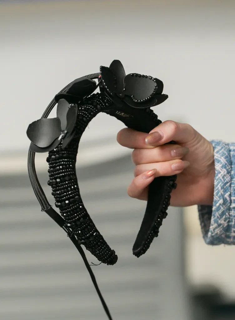 Hand holding a black beaded headband with black floral adornments, wired to a sensor.