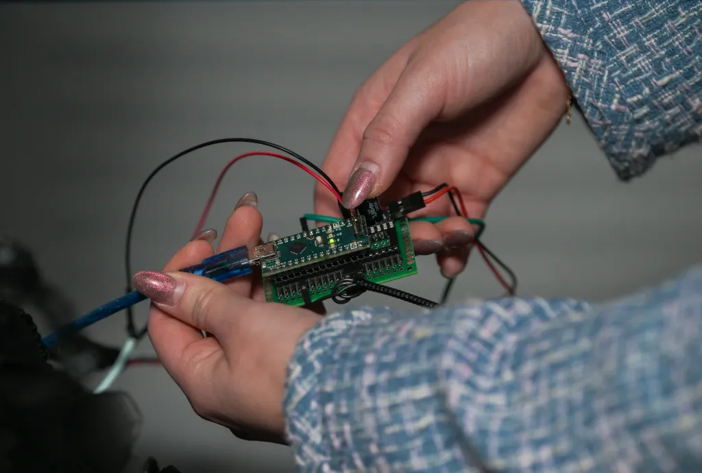 A close-up of a person connecting a blue USB cable to a small circuit board, with other wires attached to it.