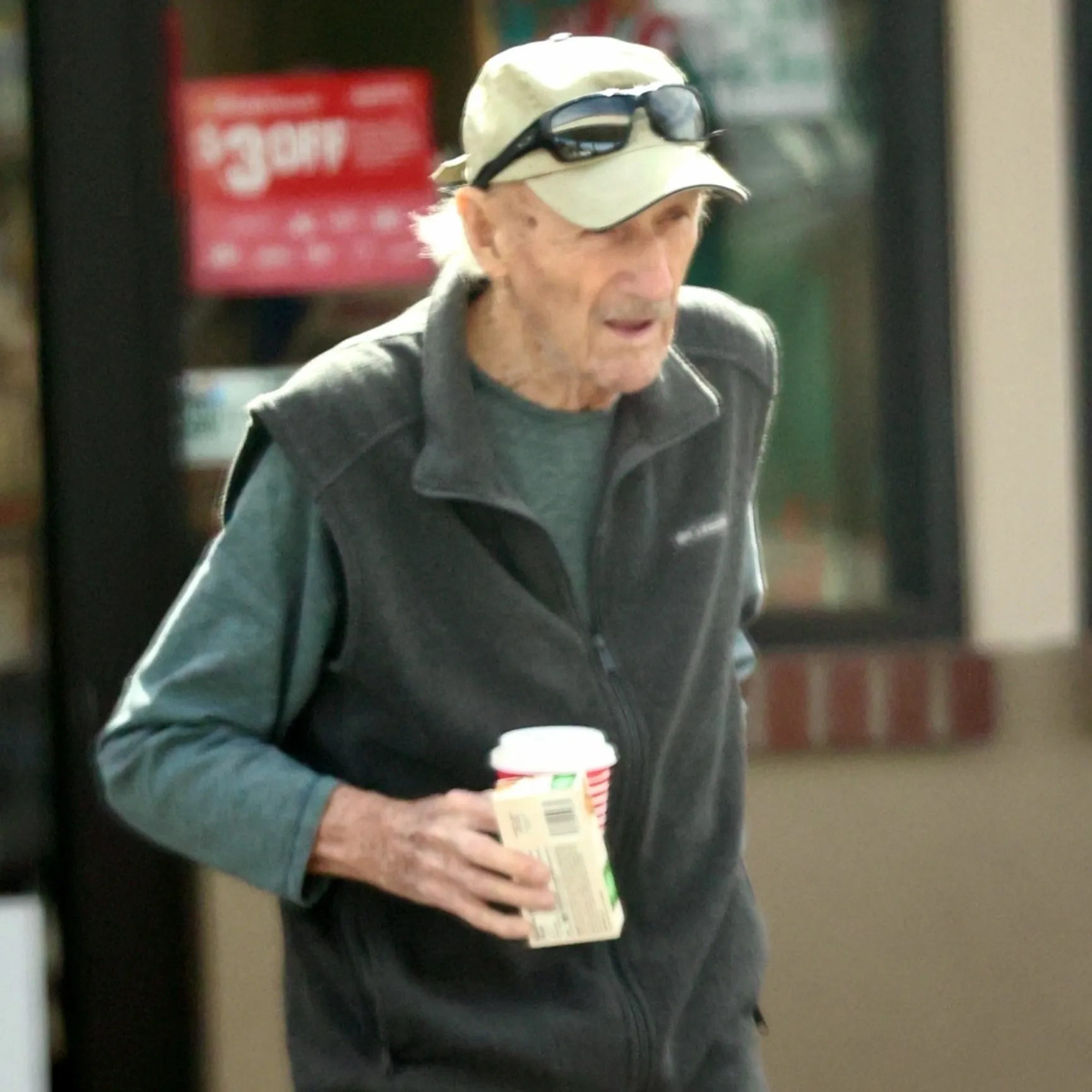Gene Hackman holding a cup and juice box while walking.