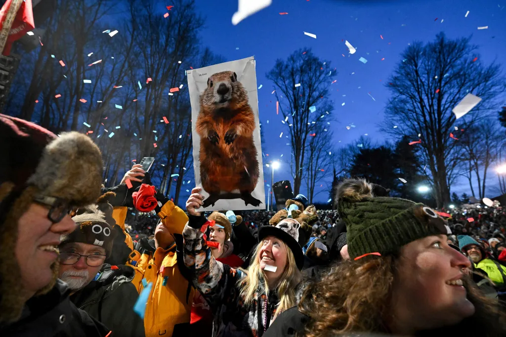 Crowd celebrating Groundhog Day with confetti and a groundhog sign.