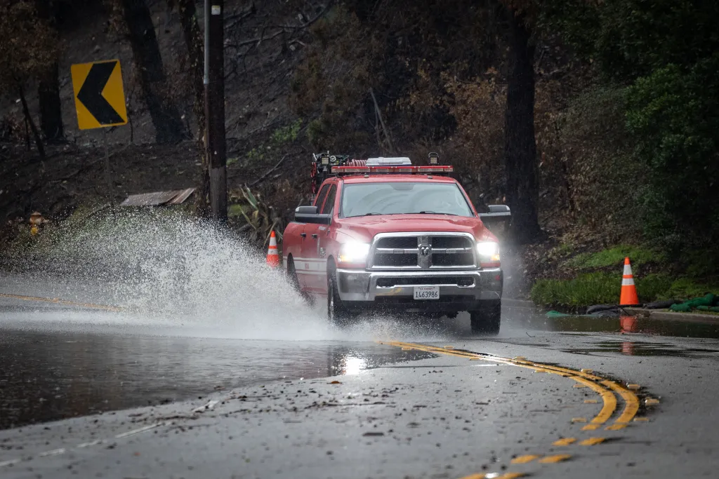 A red truck splashing through a flooded road in Los Angeles due to a dangerous storm.