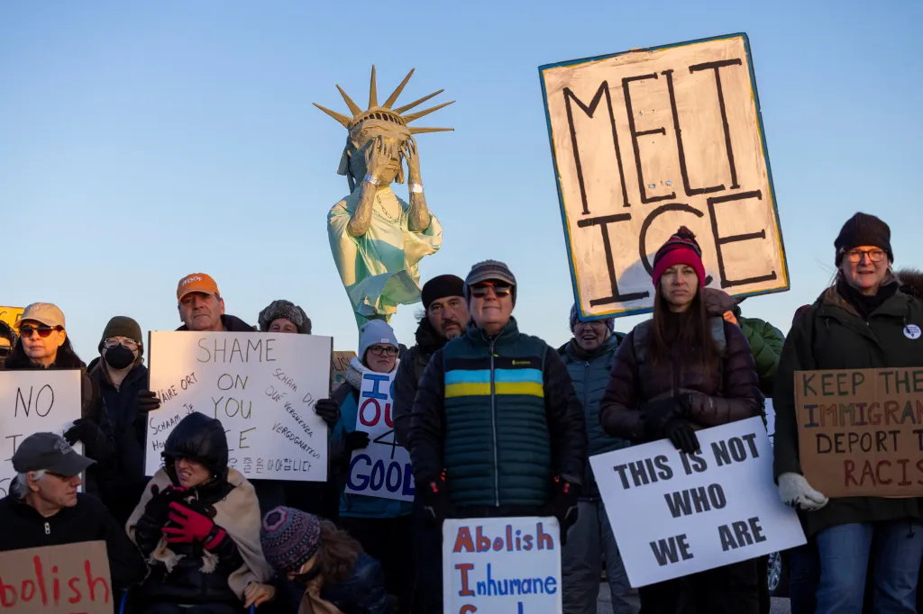 Demonstrators protest outside the Big Horn Correctional Facility with signs, one of which shows a Statue of Liberty figure covering its eyes.