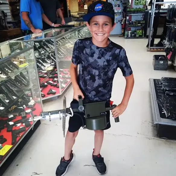 13-year-old Anthony Zecca holds a large weapon in a gun store.