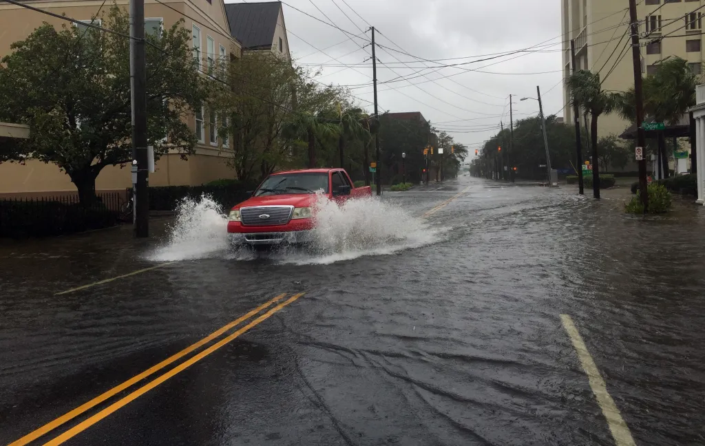 A red pickup truck drives through a flooded street, sending water splashing high in Charleston, South Carolina, due to Hurricane Dorian.