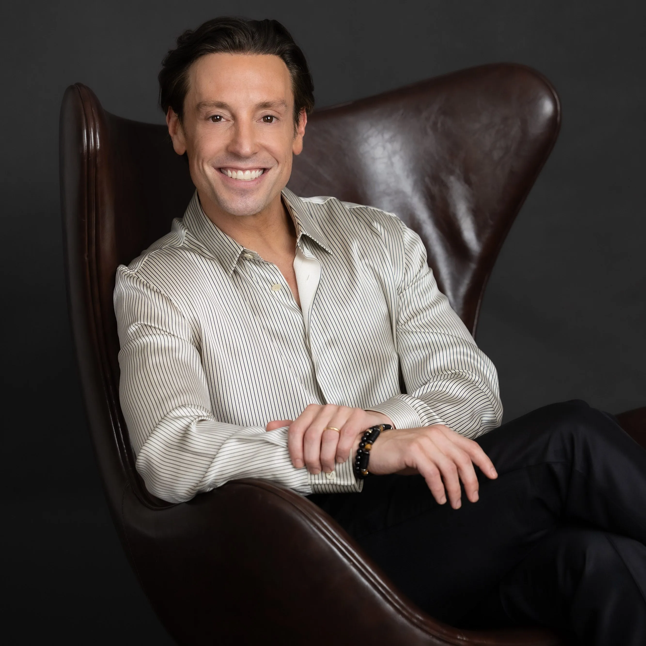 Dr. Ryan Neinstein smiling while sitting in a brown leather chair.