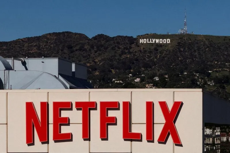The Netflix logo on a building with the Hollywood sign on a hill in the background.