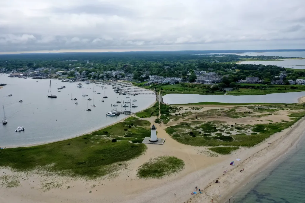 Aerial view of Edgartown Harbor Lighthouse, a town, a bay with boats, and a beach.