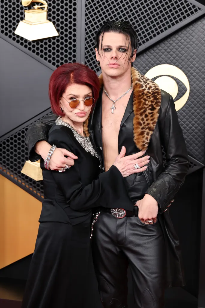 Sharon Osbourne in a black gown and Yungblud in a leather jacket and pants pose on the red carpet.