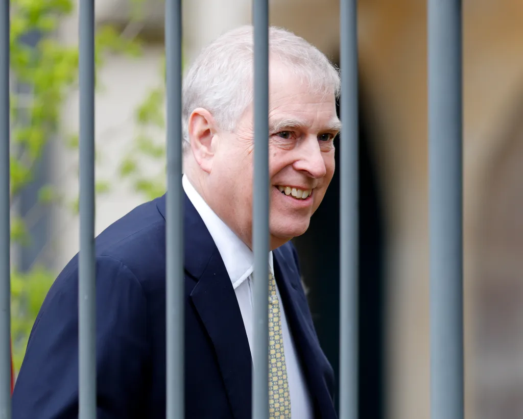 Prince Andrew, Duke of York, smiling behind metal railings.