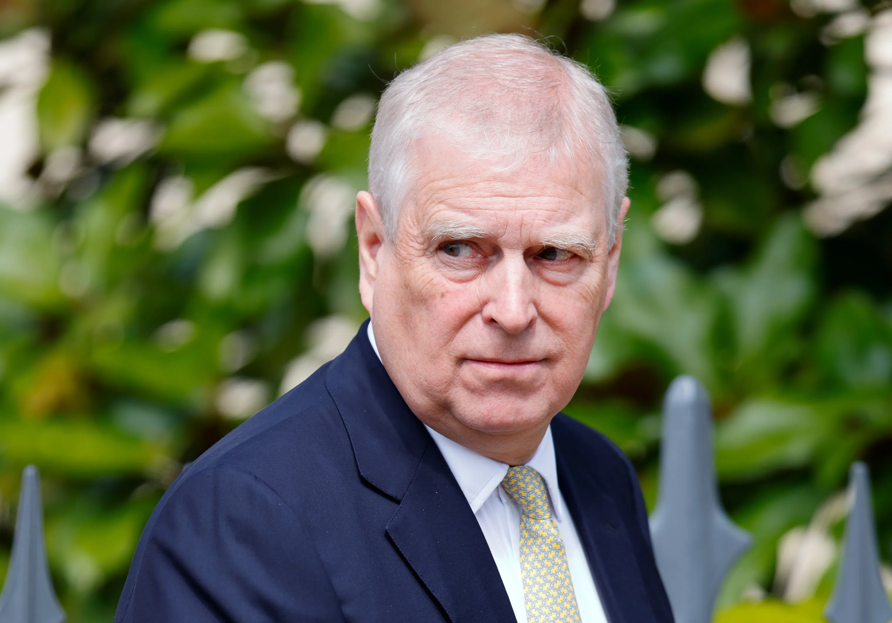 Prince Andrew, Duke of York, wearing a dark suit and yellow patterned tie.
