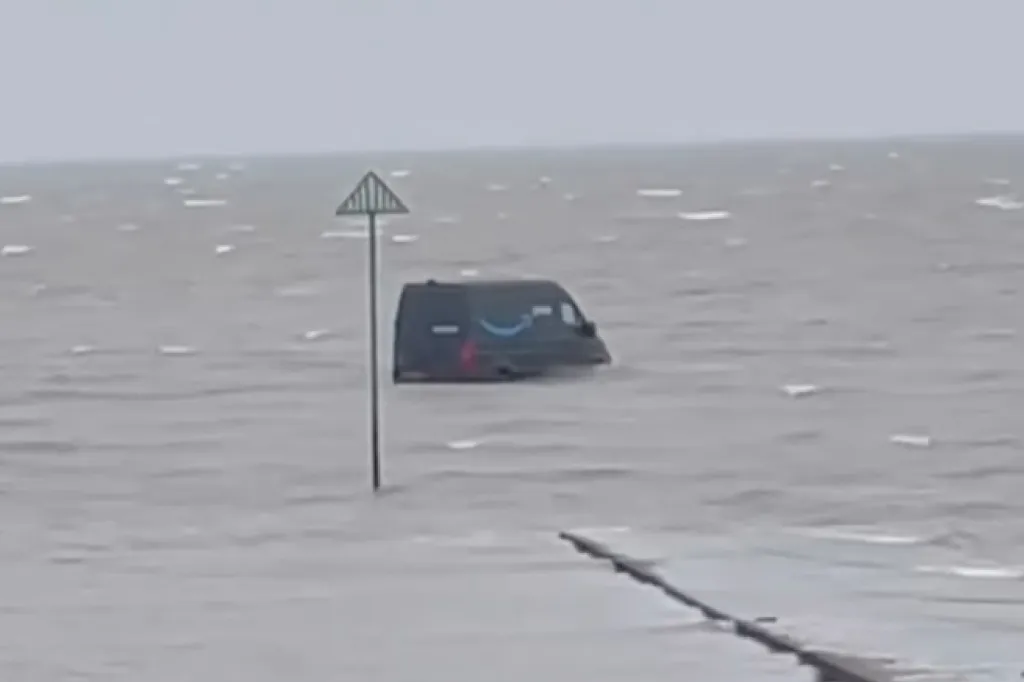 An Amazon delivery van stuck in floodwaters up to its windows, with only the top half of the van visible above the water.