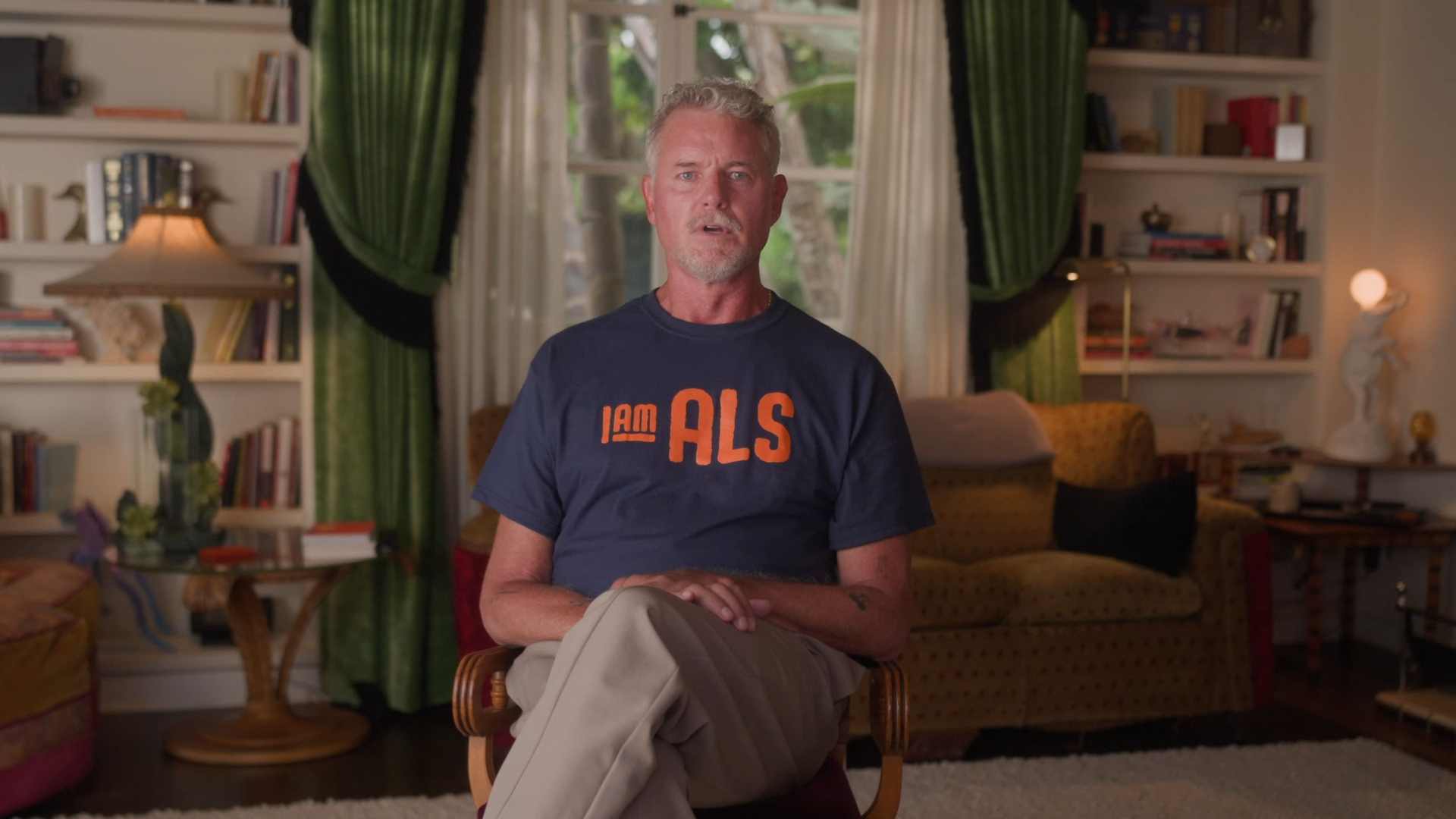 Eric Dane sitting in a living room, wearing a blue t-shirt with