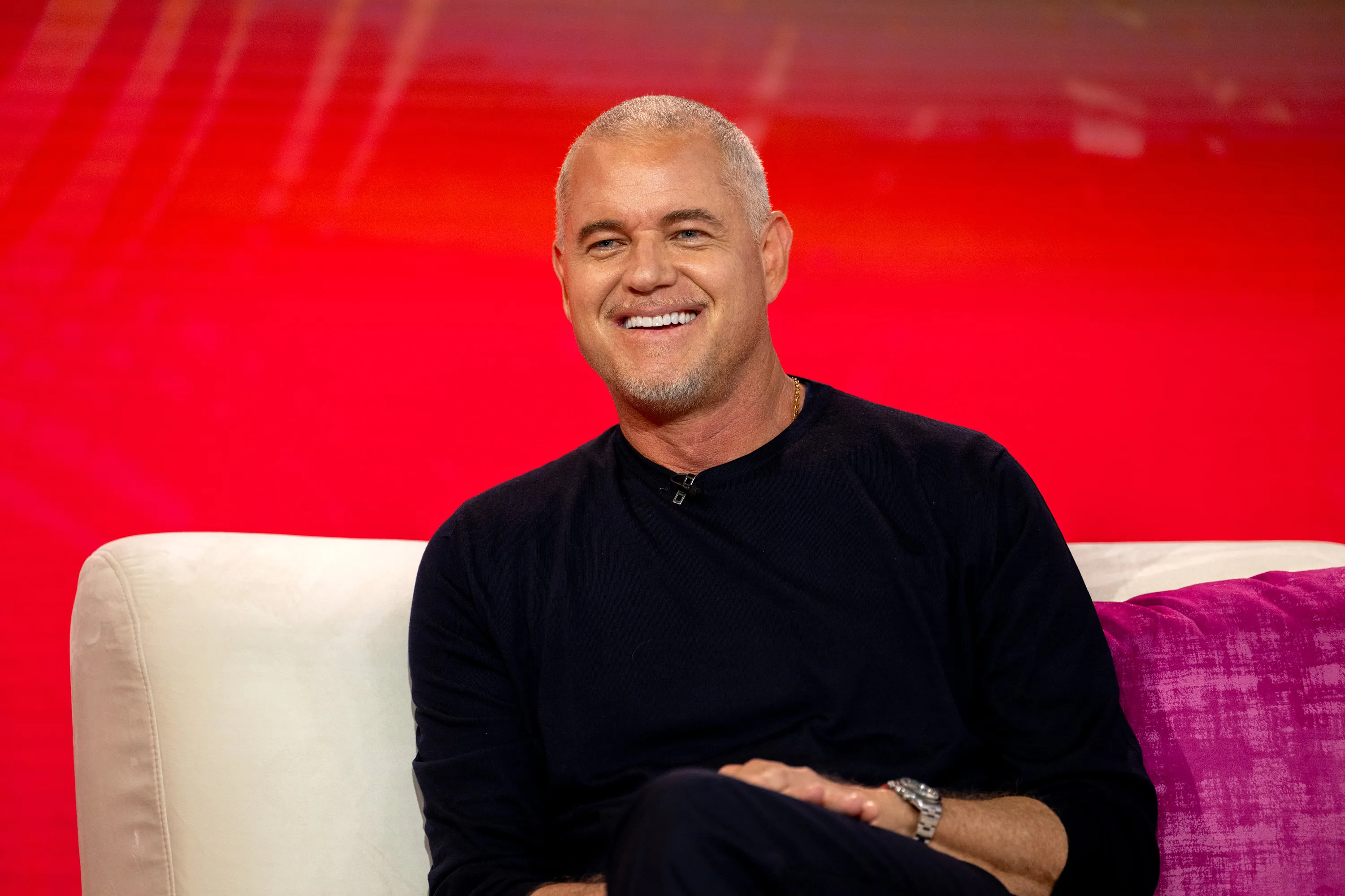 Eric Dane smiling while sitting on a couch.