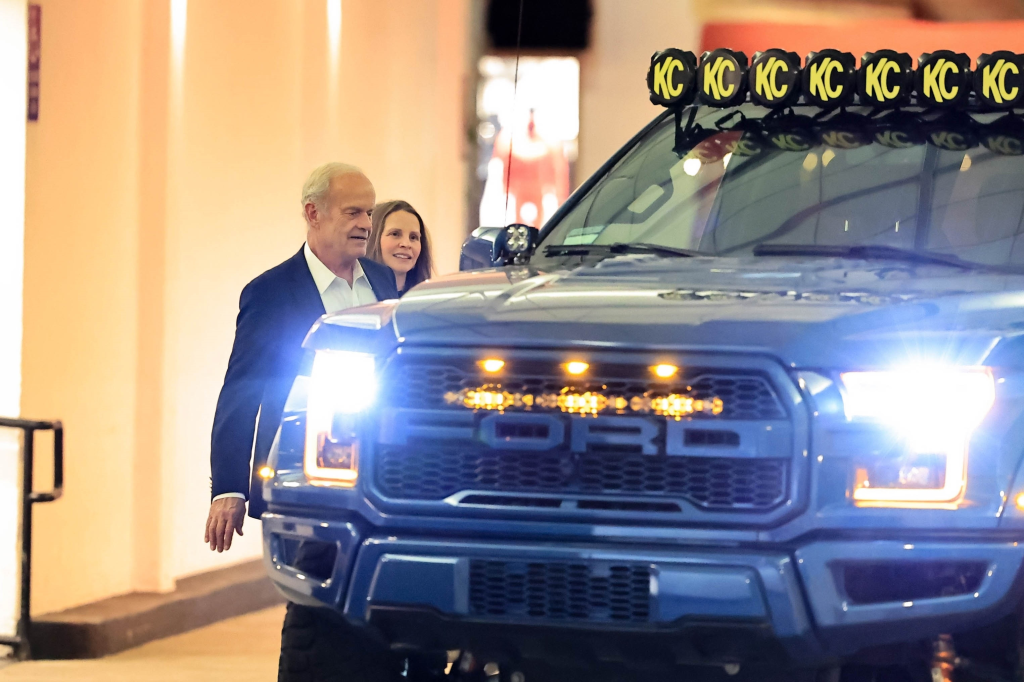 Kelsey Grammer and Kayte Walsh next to a blue Ford pickup truck with bright headlights.