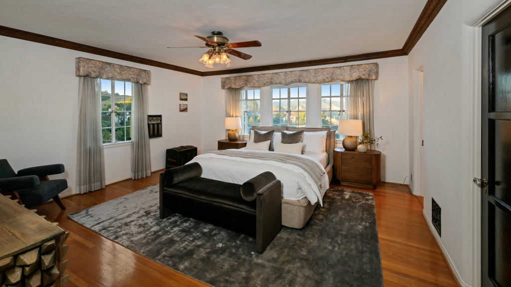 Bedroom with large windows, a king-sized bed, ceiling fan, and dark wood furniture.