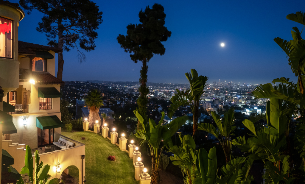 Frank Sinatra's former Los Angeles mansion and city skyline at dusk with the moon overhead.