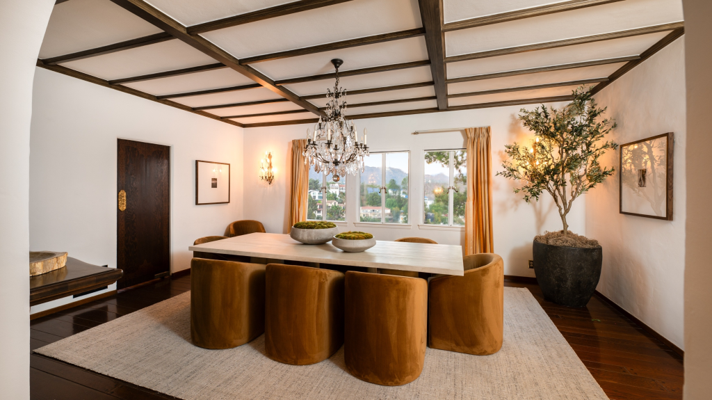 The dining room of Frank Sinatra's Los Angeles home, featuring a large wooden table with several chairs, a crystal chandelier, and large windows with a view of the city.