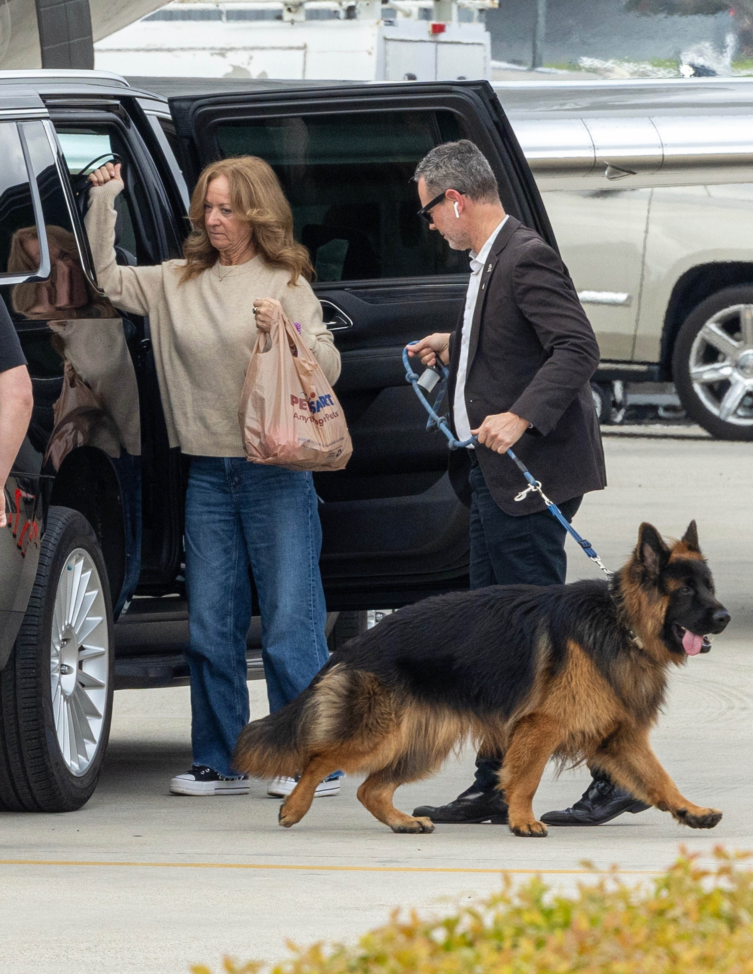 Lisa Sweeney exiting an SUV with a P.E.T. store bag while a man leads a German Shepherd on a leash.