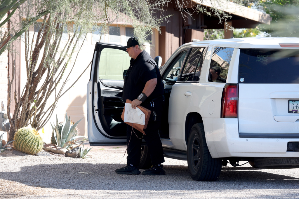 Law enforcement officer with files in hand leaving a white SUV parked in a driveway.