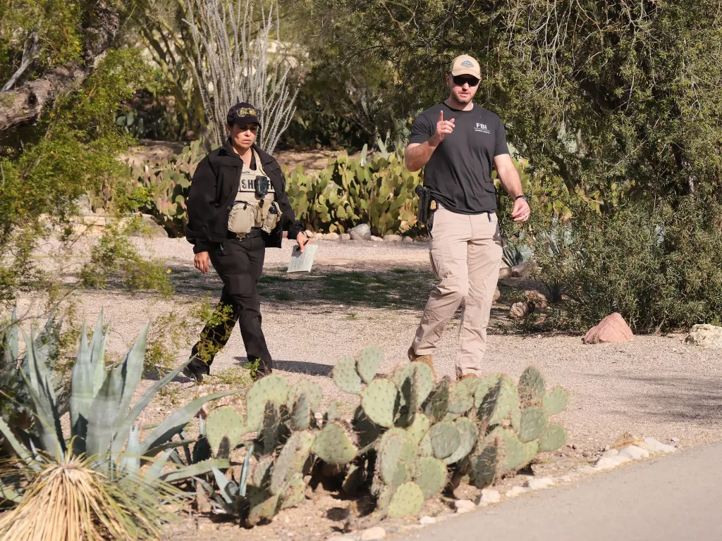 Two FBI agents walk through a desert landscape with cacti and shrubs.