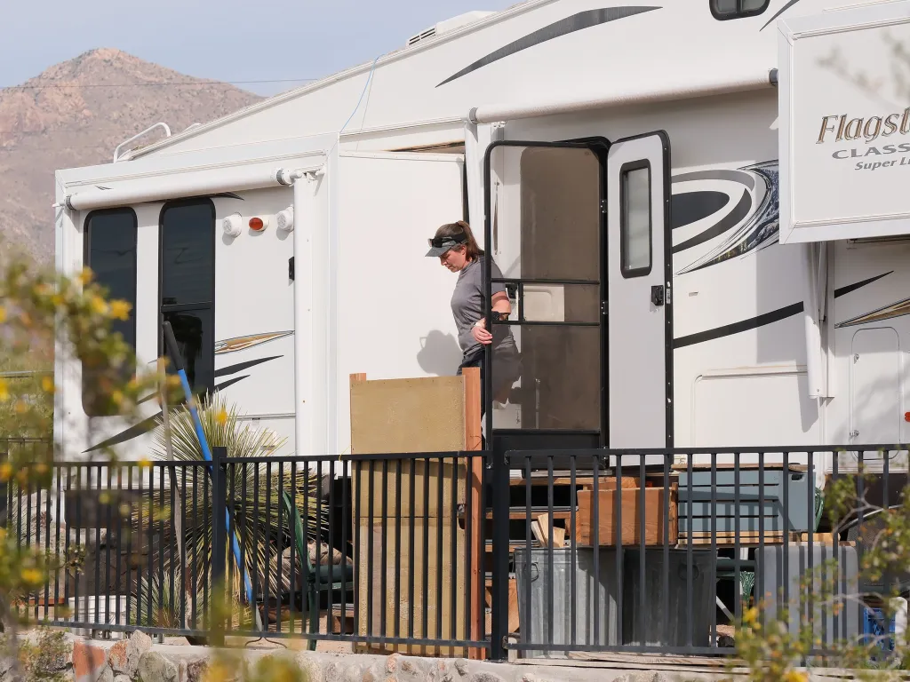 A woman in a visor and grey t-shirt stands in the open doorway of a white RV, looking down.