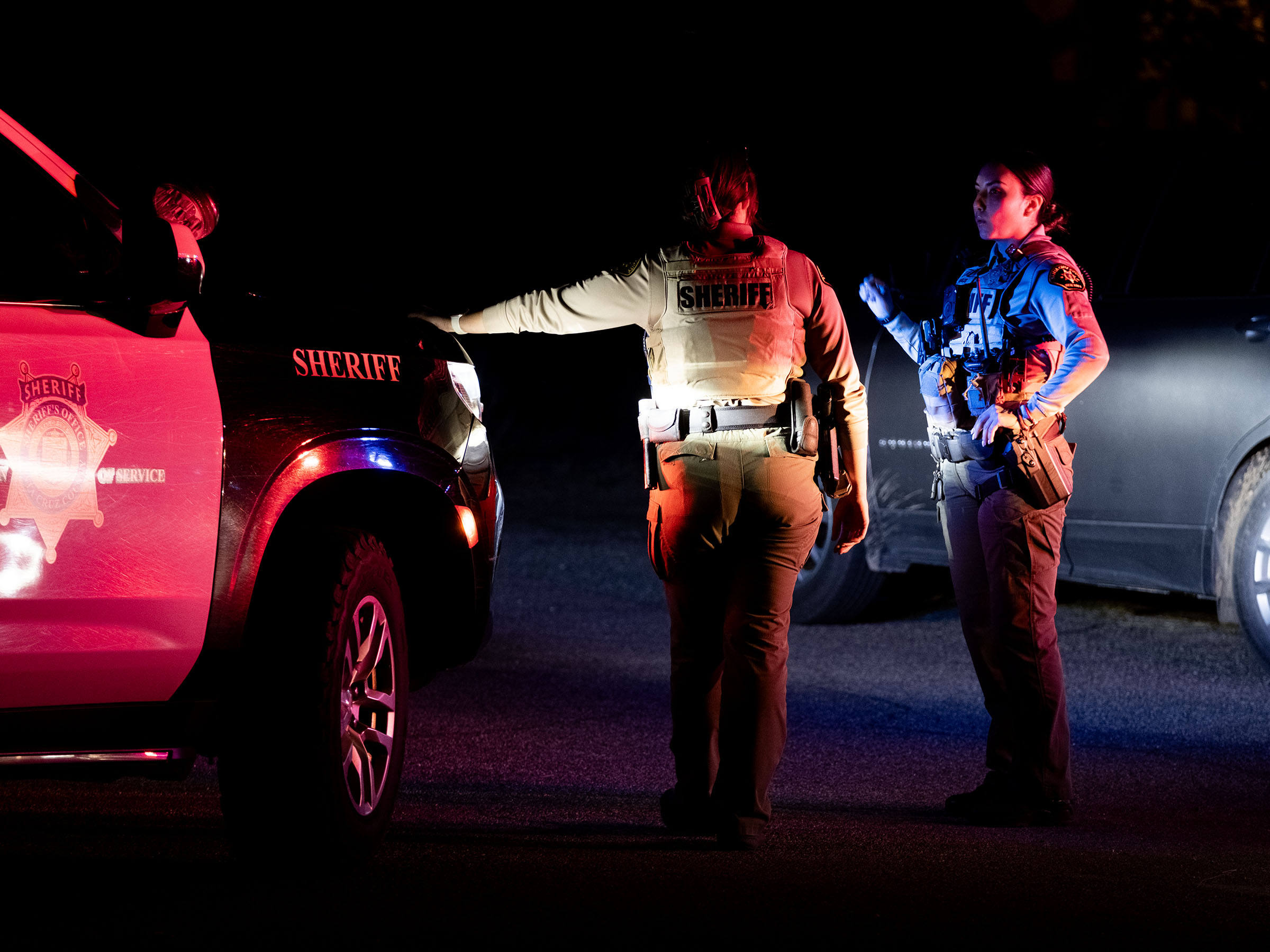 Two Sheriff's deputies and a patrol vehicle at night.