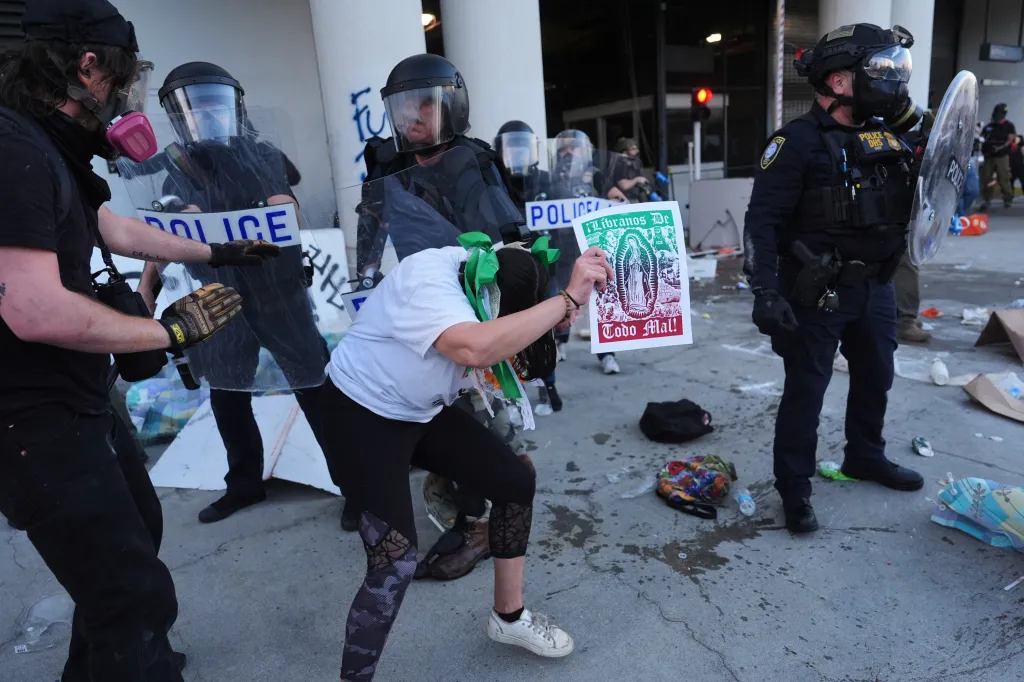 Protesters confronting federal police officers holding shields and wearing gas masks.