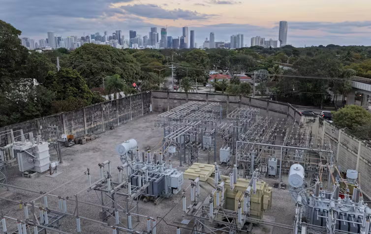 An aerial view of metal equipment and wires with a city skyline in the background.