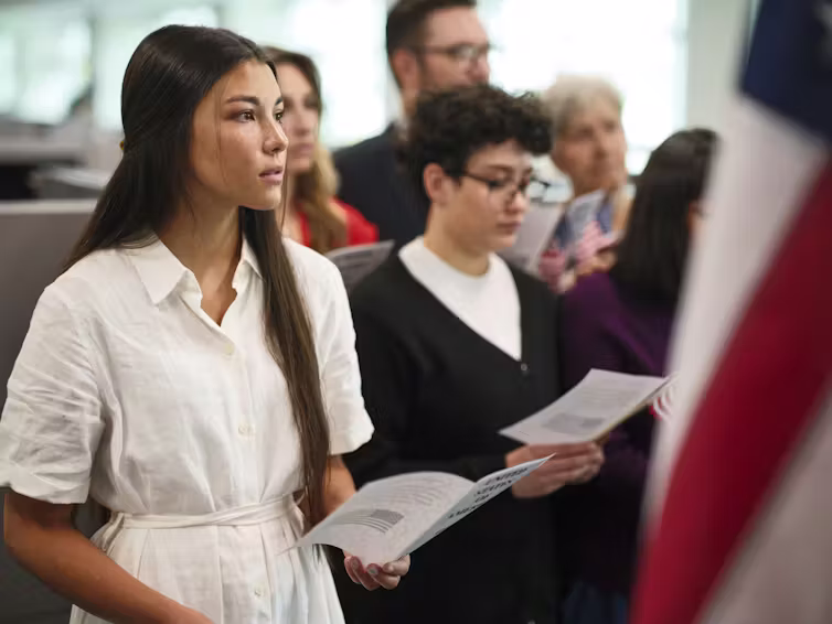 A woman holding a paper program listens attentively as part of a ceremony.