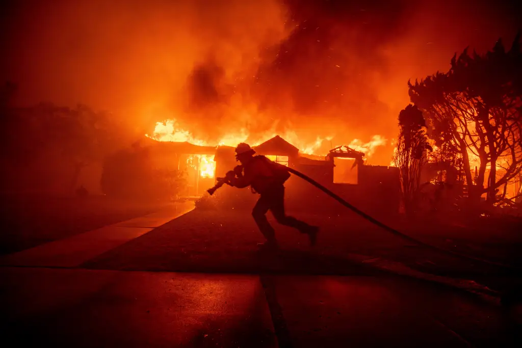 A firefighter battles the Palisades Fire as it burns a structure in the Pacific Palisades neighborhood of Los Angeles.