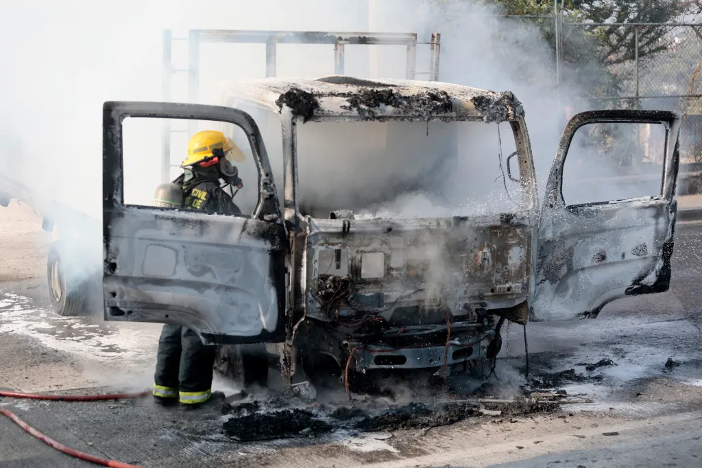 A firefighter in a yellow helmet checks a burnt truck, set on fire by organized crime groups in response to an operation in Jalisco, Mexico.