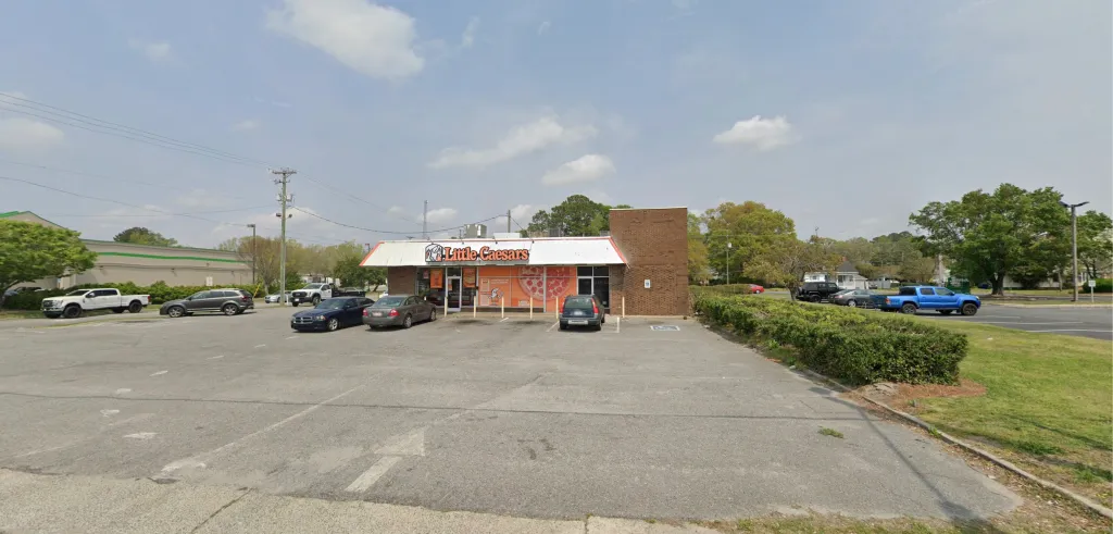 A Little Caesars restaurant with a parking lot and several cars, surrounded by trees and power lines.