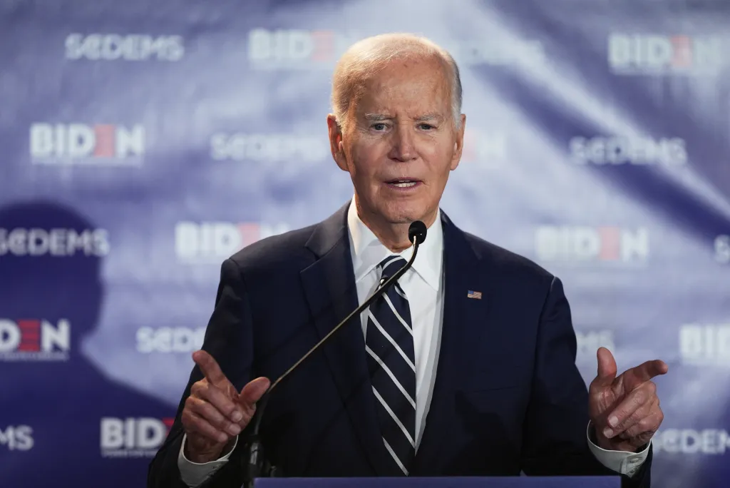 Joe Biden speaking at a podium with a blue background featuring 