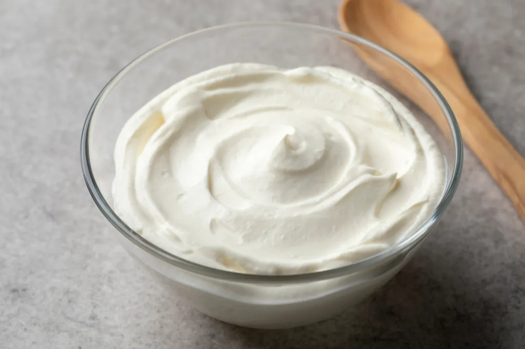 Creme fraiche in a glass bowl next to a wooden spoon.