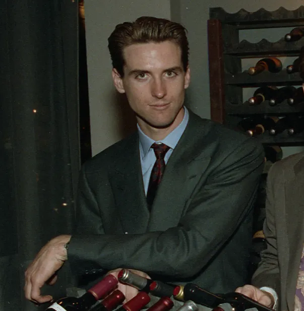 Gavin Newsom stands in a suit and tie, leaning on a stack of wine bottles at the opening of PlumpJack wine shop.