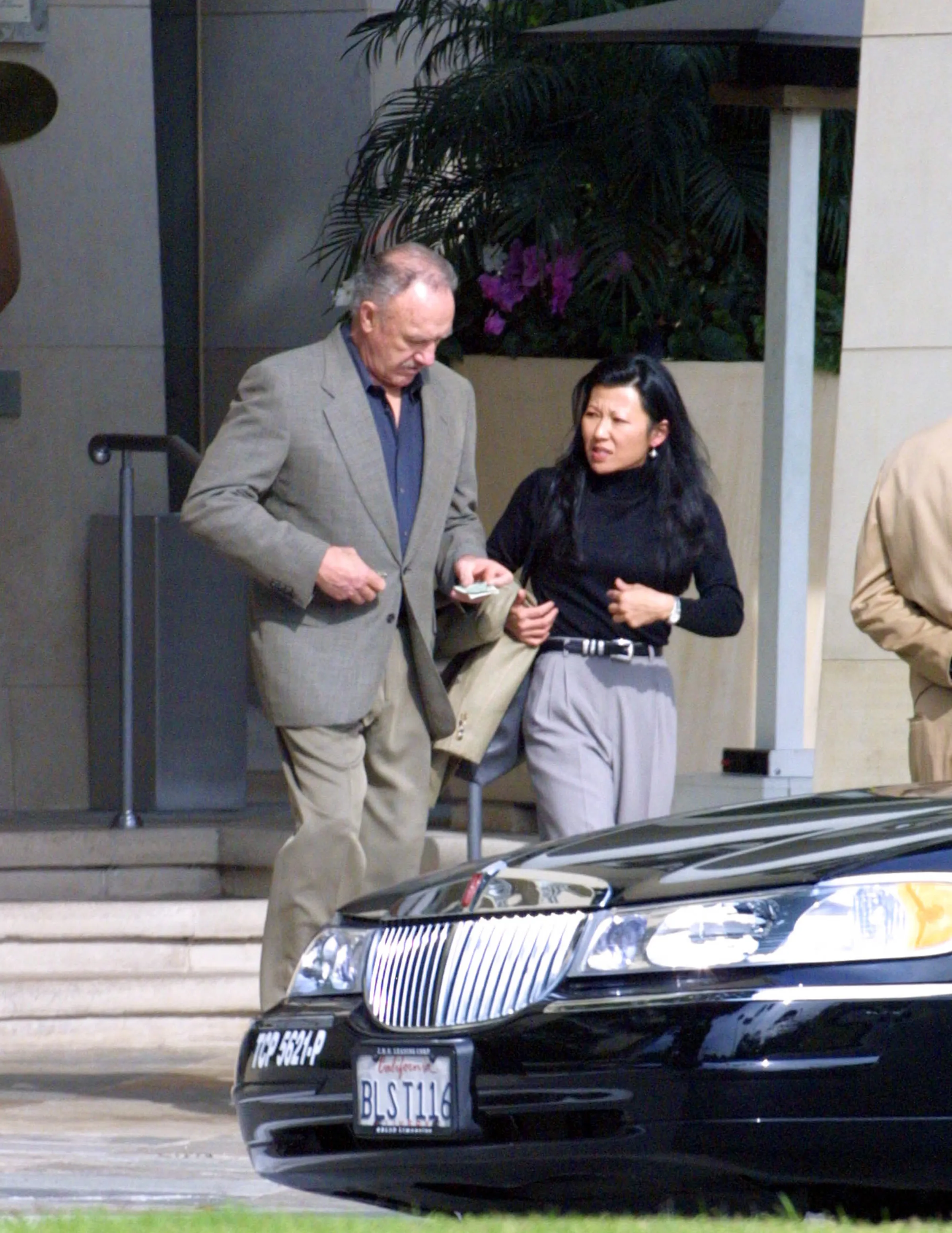 Gene Hackman hands money to Betsy Arakawa next to a black car.