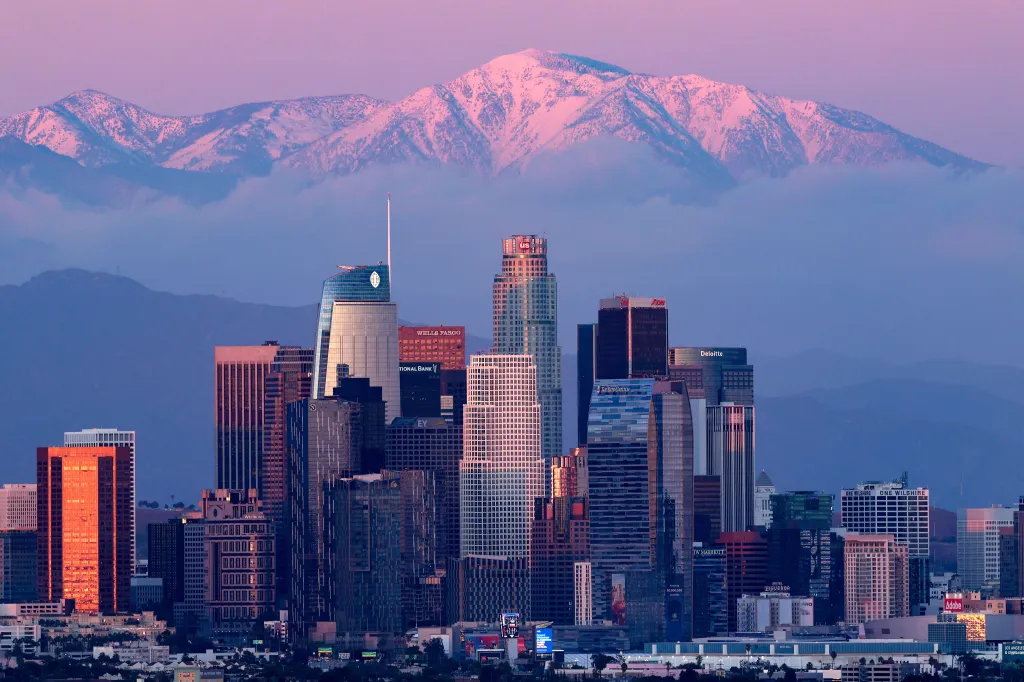 Los Angeles skyline with snow-capped mountains in the background at sunset.