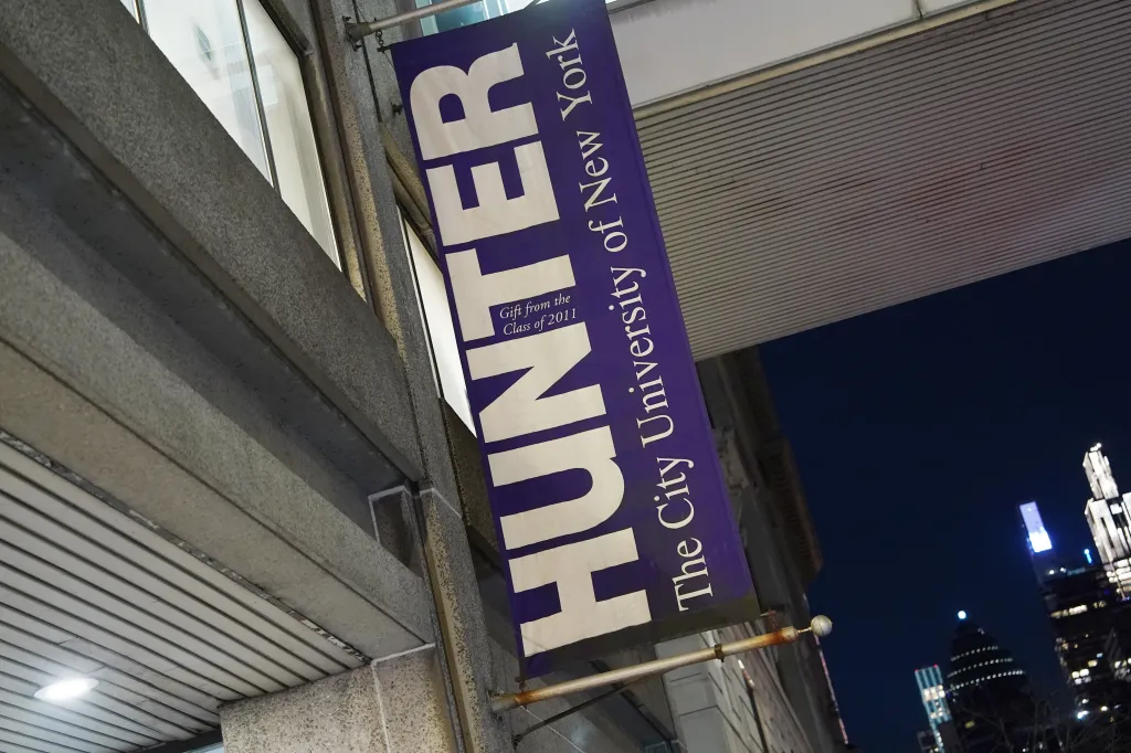 A banner for Hunter College, The City University of New York, hanging from a building at night.