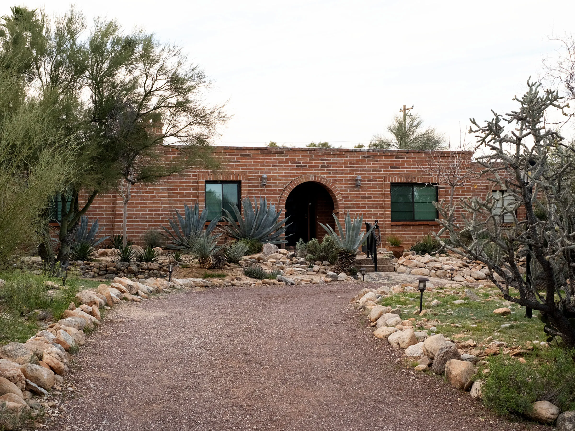 The exterior of Nancy Guthrie's brick home in Tucson, Arizona, with a gravel driveway leading to an arched entry and desert landscaping.