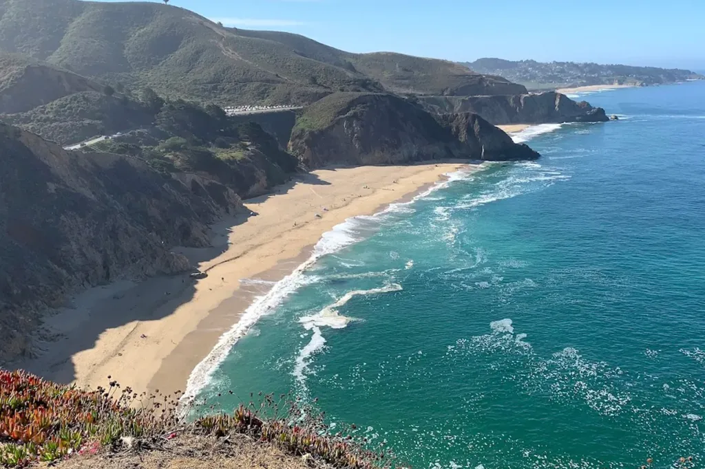 Gray Whale Cove State Beach in San Mateo County, California, with ocean waves breaking on the sandy shore and cliffs rising above.