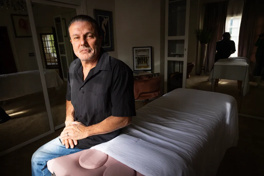Frank Santangelo sits on the massage table where his wife received a fatal silicone injection.