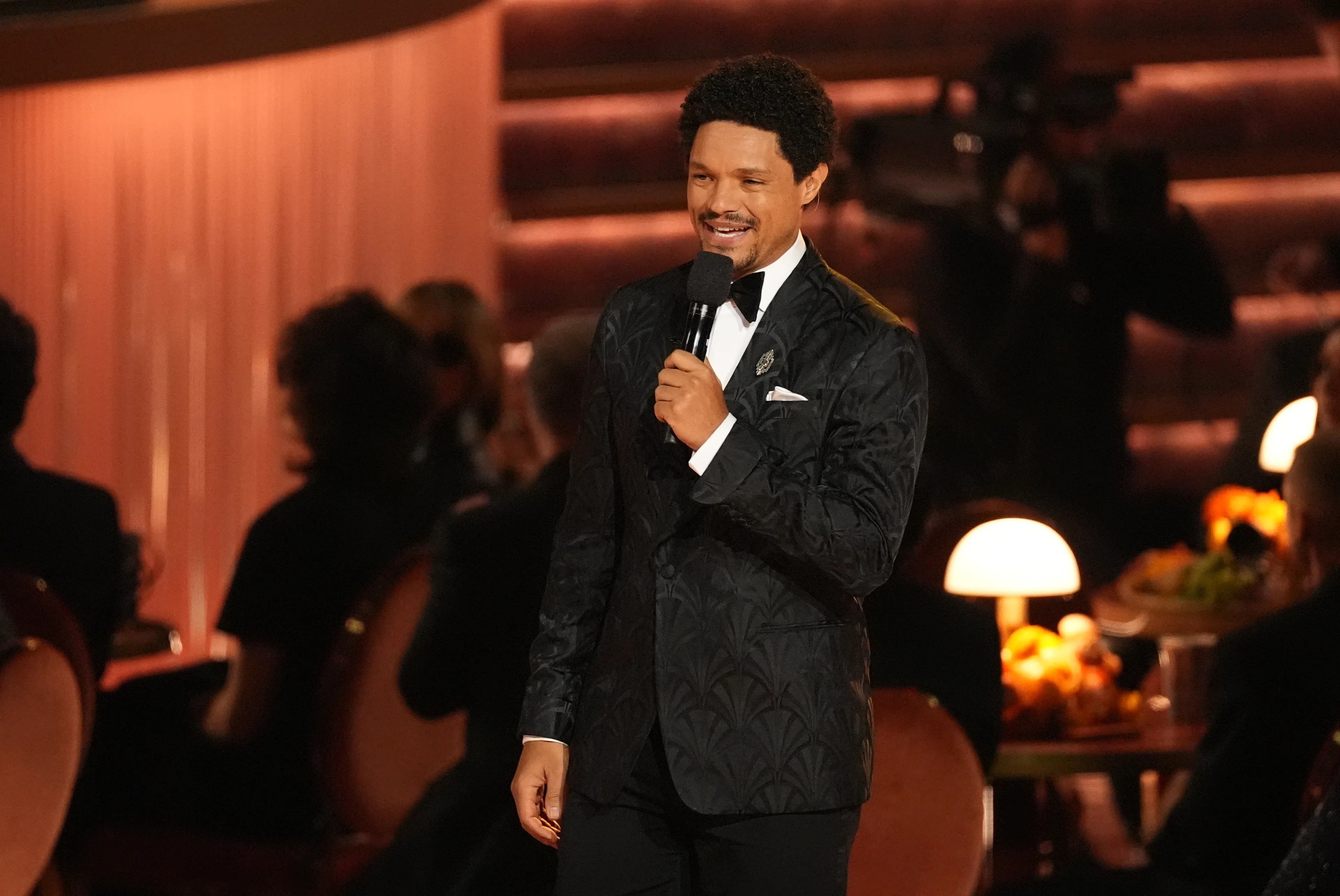 Trevor Noah at the Grammys onstage, holding a mike