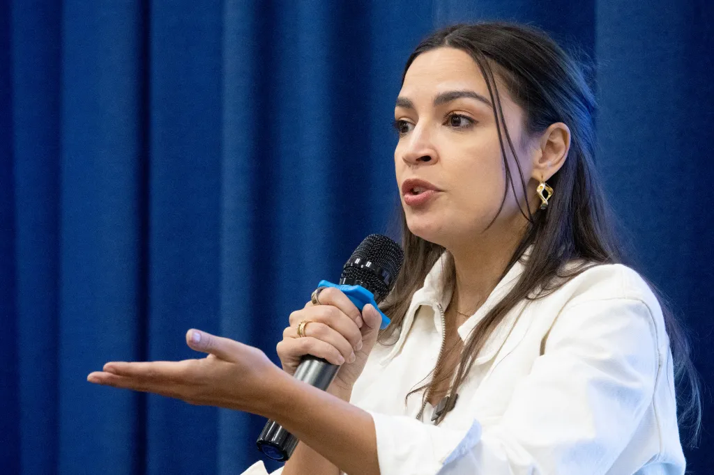Rep. Alexandria Ocasio-Cortez speaking into a microphone at a town hall in Queens.
