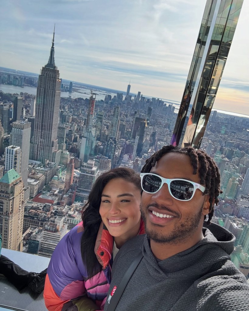 Victoria and Antonio Gibson taking a selfie together with the New York City skyline and Empire State Building in the background.
