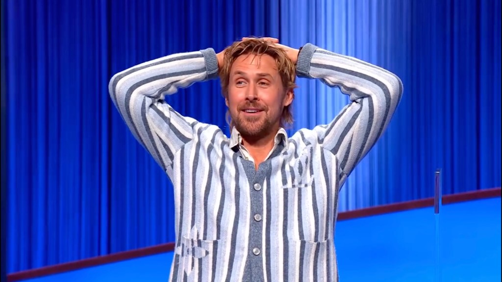 Ryan Gosling with his hands on his head in a striped cardigan.