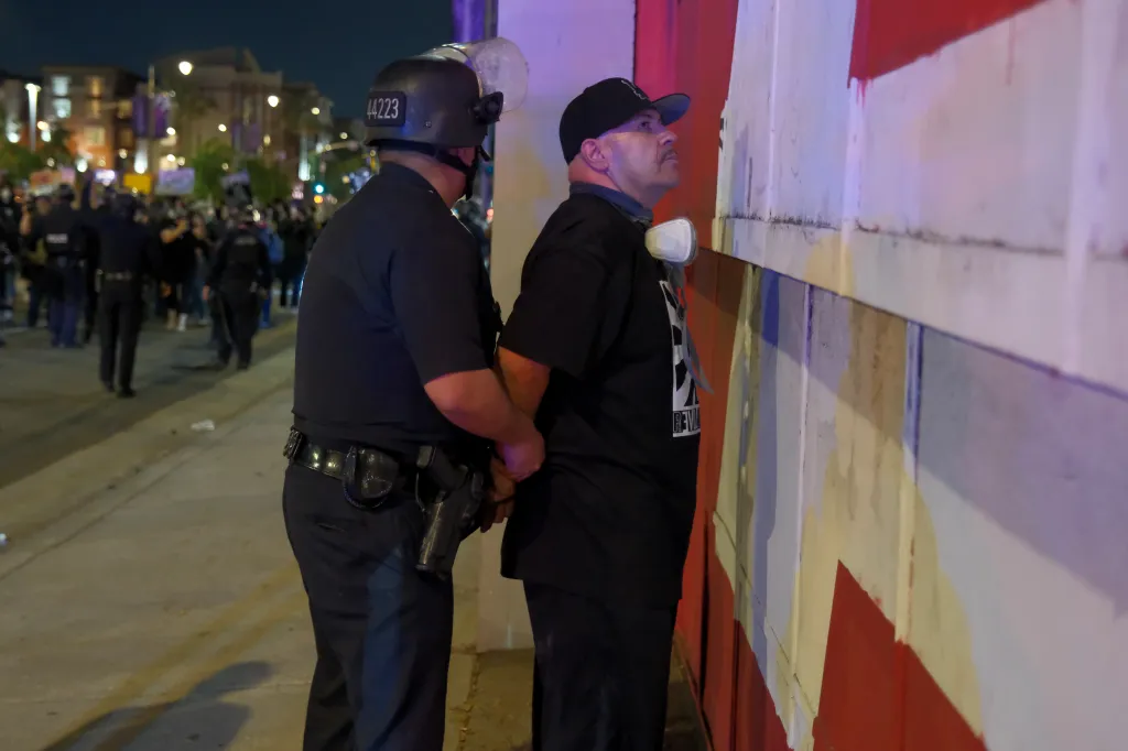 A police officer handcuffs a protester against a painted wall during an ICE protest in Downtown LA.