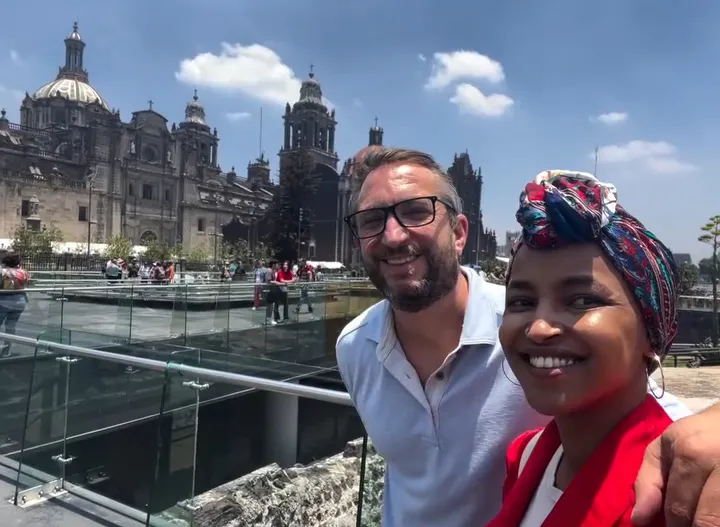 Ilhan Omar and Tim Mynett smiling for a selfie in front of a cathedral.