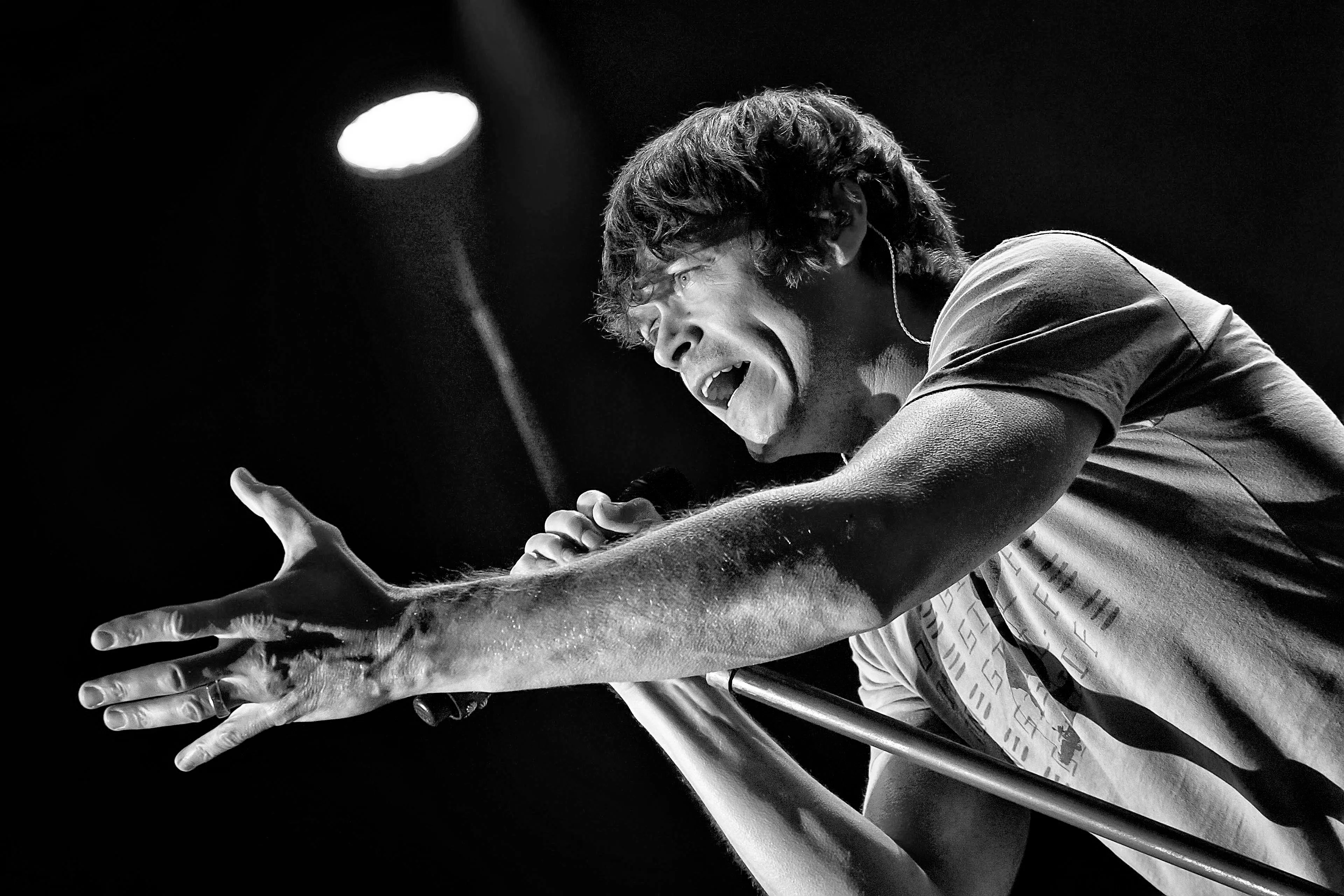 Black and white photo of Brad Arnold singing into a microphone on stage, with one hand outstretched.