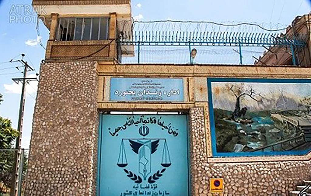 The entrance to Bojnourd Prison in Iran, featuring a gate with the scales of justice emblem and a guard tower above.